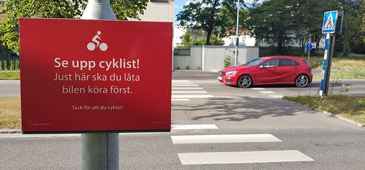 Tillfällig skylt vid ett övergångsställe - uppmanar cyklisten att stanna för mötande bilar
