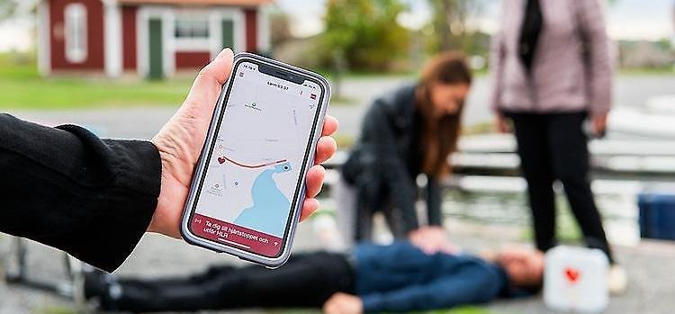 Telefon med app som kontaktar sjukvård medan livräddning pågår i bakgrunden