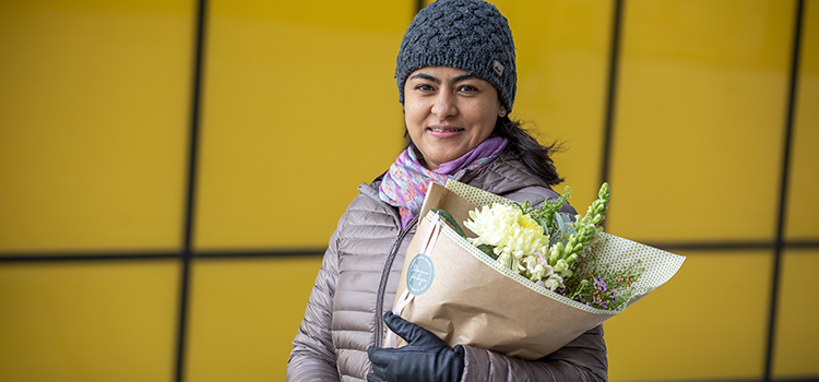 Laura Ferrans står framför den gula universitetsbyggnaden Stella med blommor i famnen.
