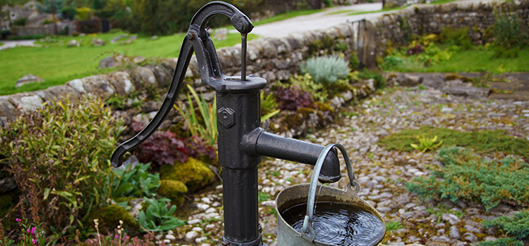 Bilden visar en gammaldags vattenpump som precis fyllt en vattenkanna