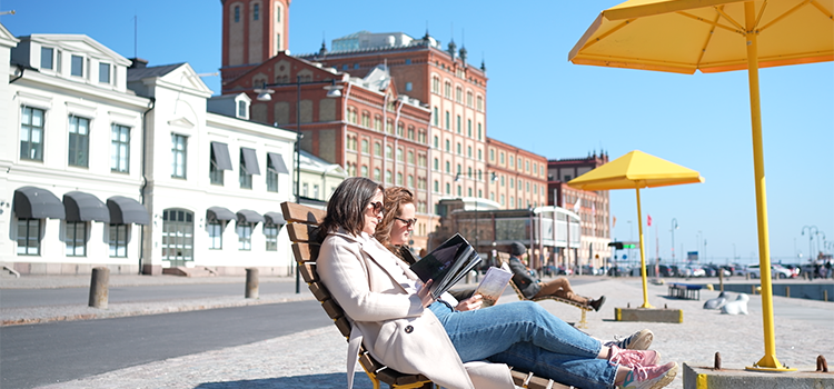 Två kvinnor sitter och läser bok på en gul bänk under gula parasoll vid Elevatorskajen i Kalmar