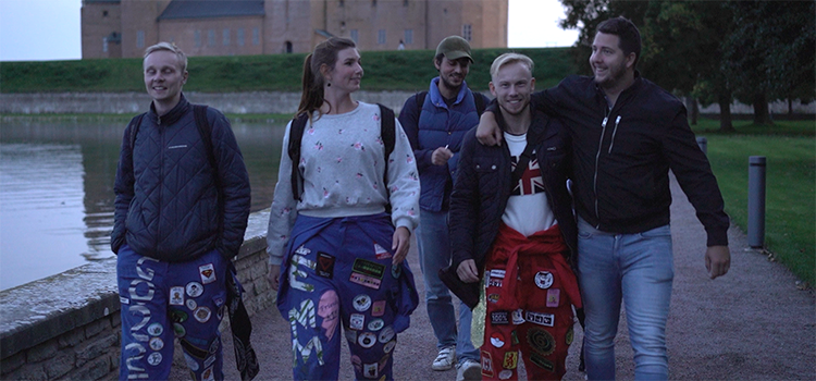Fem studenter, några i studentoverall, några i vanliga kläder, går tillsammans i kvällsljus med Kalmar slott i bakgrunden