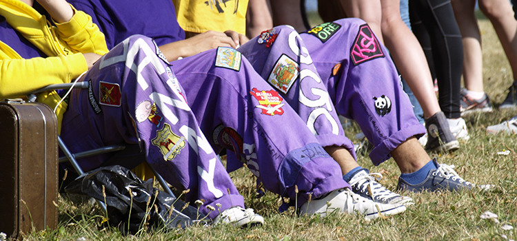 Studenter sitter i gräset med lila overaller. Bara benen syns.