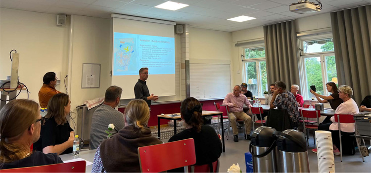 Samling av människor i en lokal som lyssnar på en presentation.