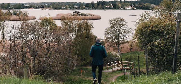 Man går ner för en brant stig. Framför sig har han utsikt över Västra sjön, ett av Kalmartraktens få skärgårdslikande områden. 