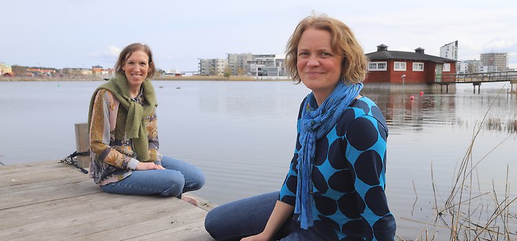 Två kvinnor sitter på en brygga med Klapphuset i bakgrunden.