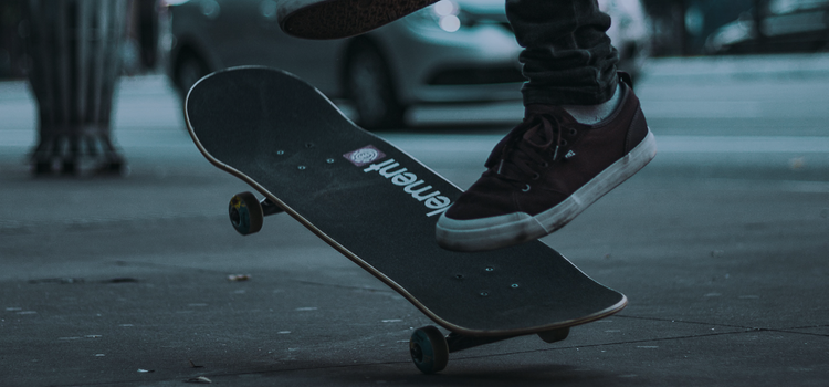 Närbild på en skoklädda fötter ovanför en skateboard som hänger i luften, mitt i ett hopp. 